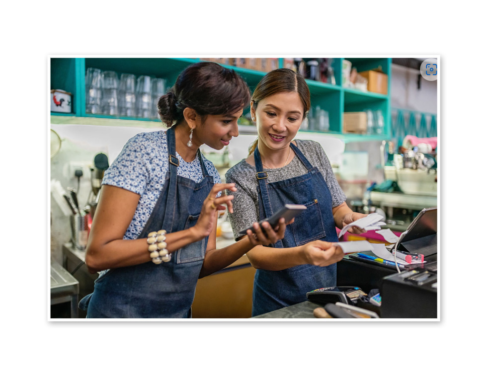 Two employees standing together and looking at one of their cell phones.