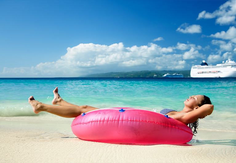 Person sitting in a pink floaty on a beach.