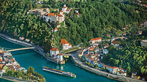 Aerial view of a riverside town with a castle, river, and cruise boat.